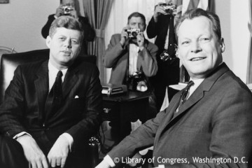 Willy Brandt sitzt neben US-Präsidenten John F. Kennedy im Weißen Haus. Fotografie in Schwarz-Weiß. Öffnet weitere Informationen zu den deutsch- amerikanischen Beziehungen.