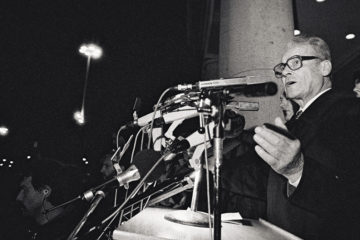 Schwarz-Weiß-Aufnahme von Willy Brandt aus dem Jahre 1989 vor einer Vielzahl von Mikrofonen bei einer Kundgebung vor dem Rathaus Schöneberg zum Fall der Berliner Mauer.